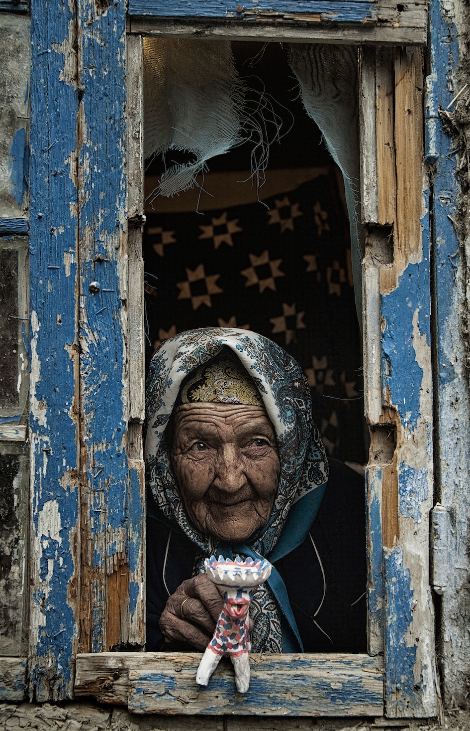 An old lady at the window with a toy in her hands
