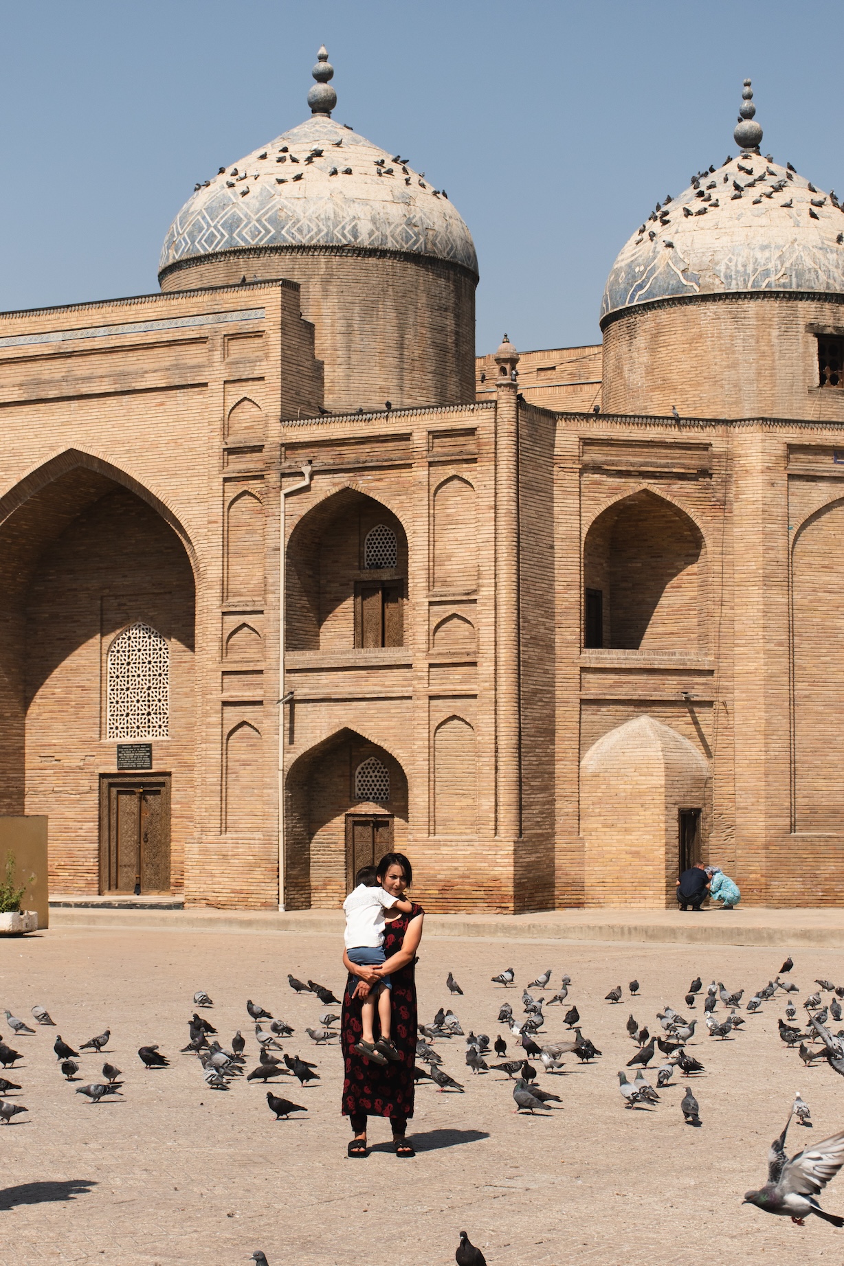 Une mère porte son enfant, debout au milieu de dizaines de pigeons, devant le mausolée du cheikh Muslihiddin à Khodjent.